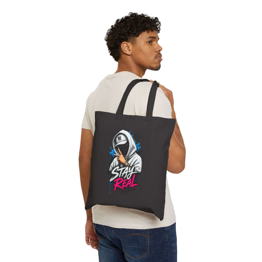 Durable cotton canvas tote bag featuring a stylish graphic design with the phrase 'Stay Real' on a black background.